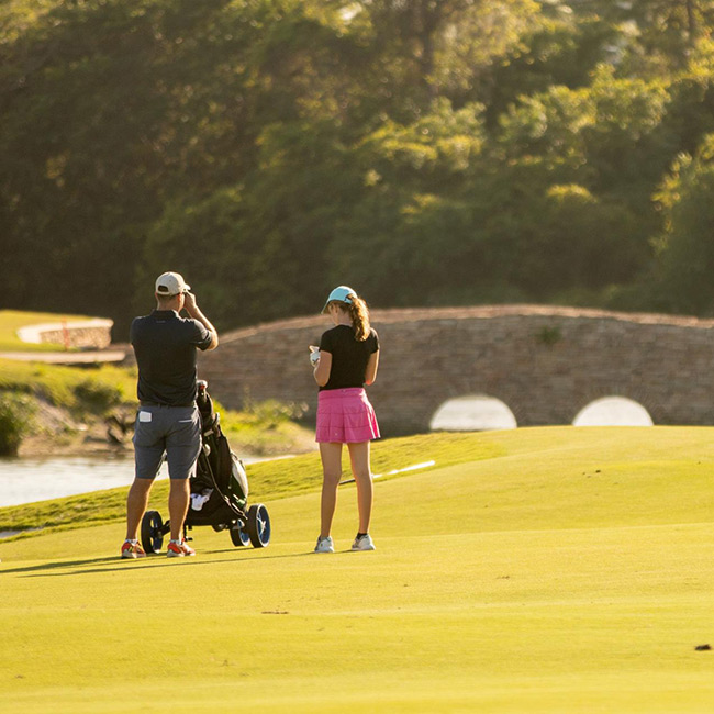 Golfers beside a stone bridge at Broken Sound Club
